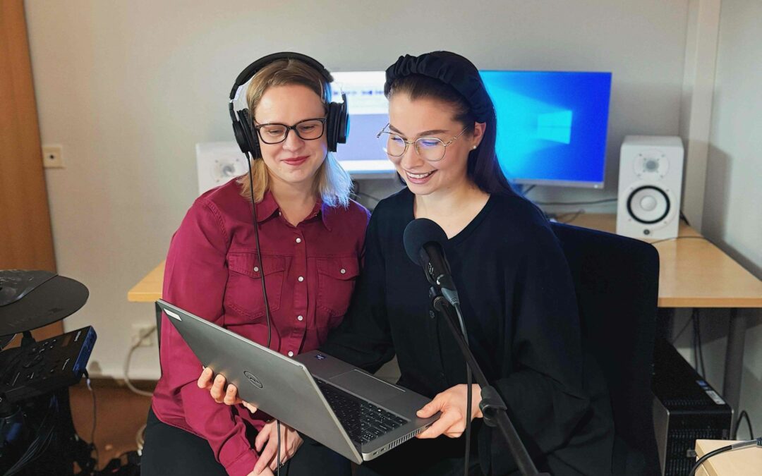 Kaksi naista kuulokkeet korvilla katsovat kannettavaa tietokonetta studiossa.