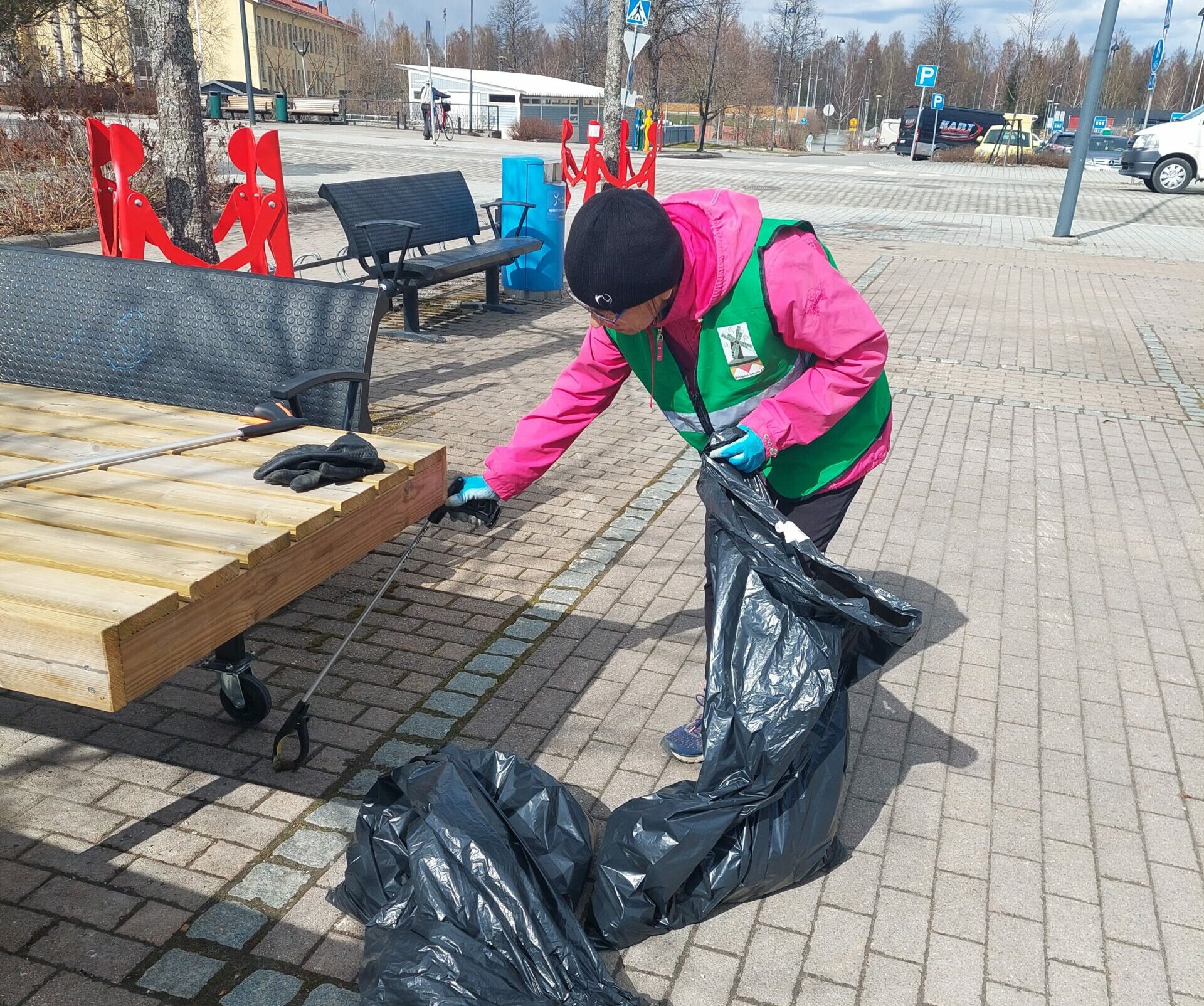 Nainen kerää roskapihdeillä roskia jätesäkkiin.