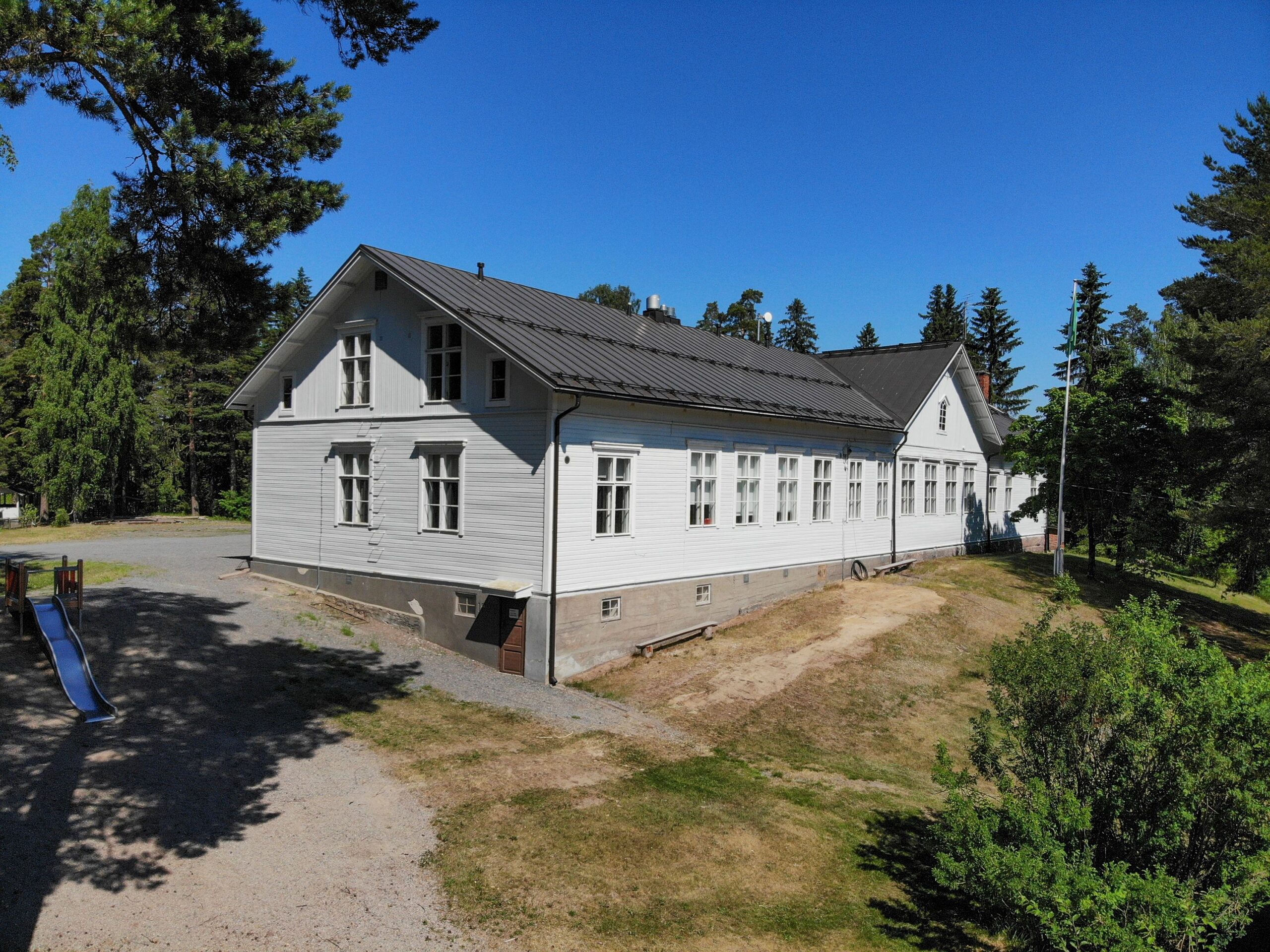 Valkoinen koulurakennus aurinkoisessa säässä.