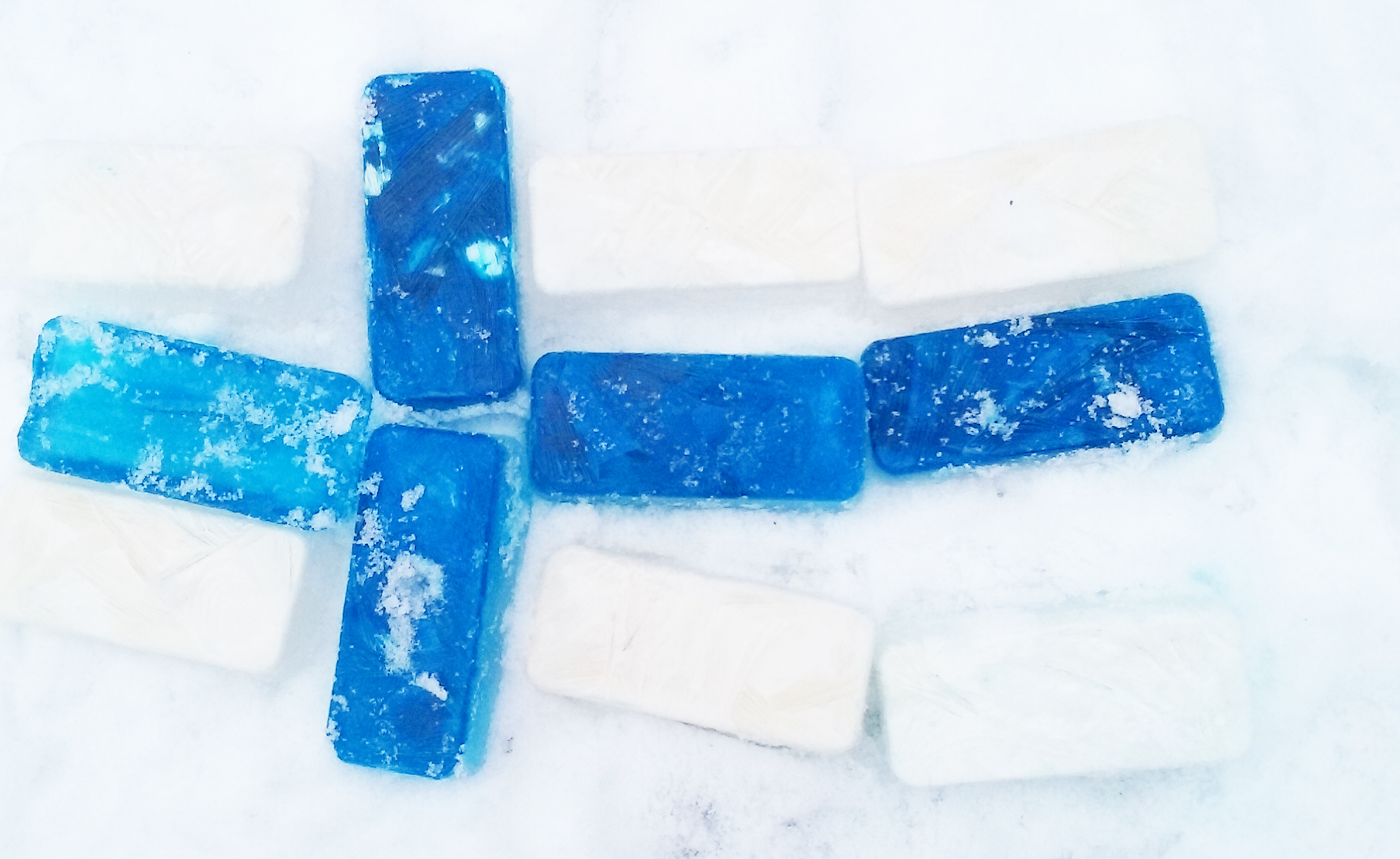 Lumiseen maahan tehty valkoisista ja sinisistä jääpalikoista Suomen  lippu.