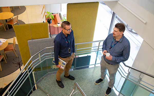 Kaksi miestä keskustelee toimiston portaissa ylhäältä kuvattuna.